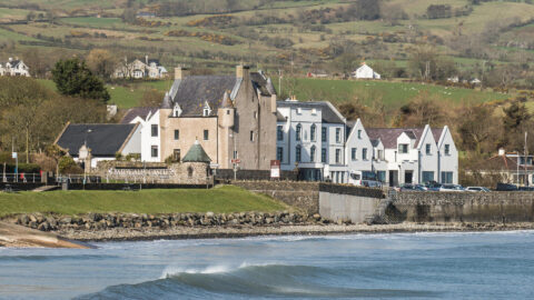 Stunning castle hotel by the sea with lush green hills, offering coastal charm and historic elegance.