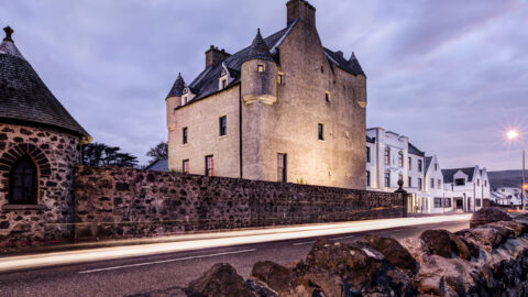 Historic stone hotel at dusk, warm lights, cosy atmosphere, scenic street, enchanting architecture, inviting stay in Scotland.