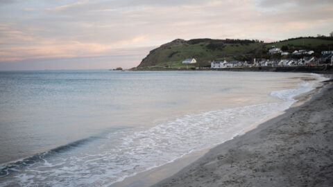 Serene beach view with gentle waves, coastal village and rolling hills, offering a peaceful retreat and scenic walks.