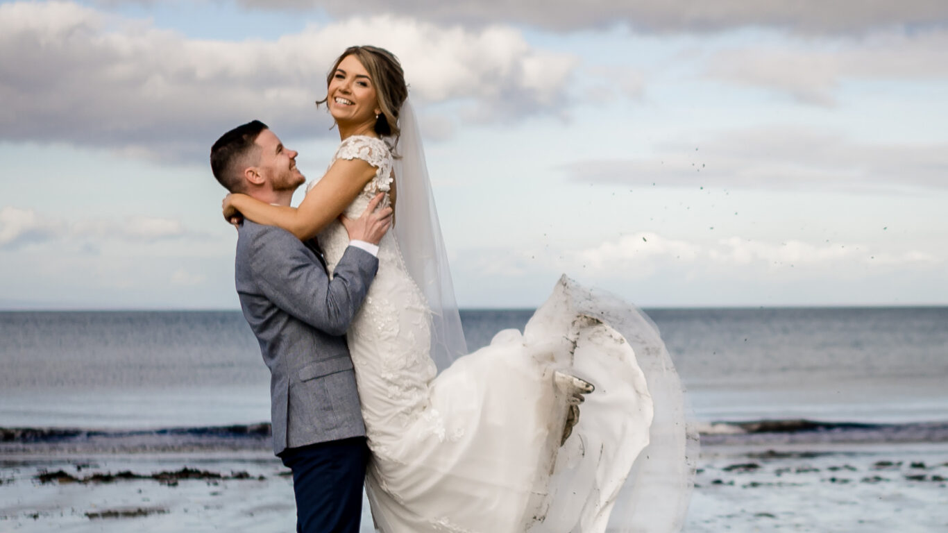 A joyful couple embrace on a sandy beach with dramatic skies, creating perfect wedding memories by the sea.