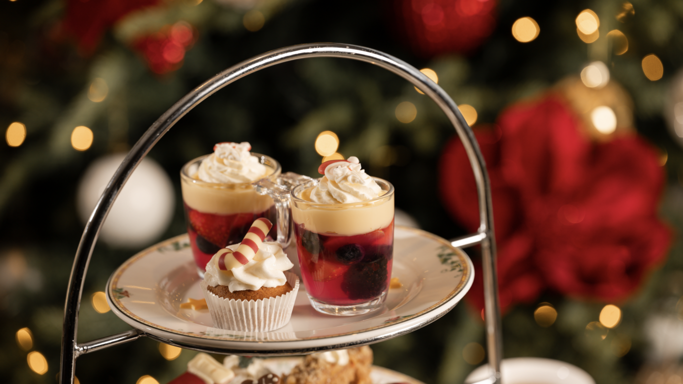 Festive afternoon tea at hotel with seasonal cupcakes and berry parfaits, against a glowing Christmas tree backdrop.