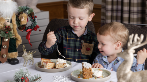 Two young boys enjoy festive cake at a Christmas-themed hotel dining table, decorated with reindeer and Santa figurines.