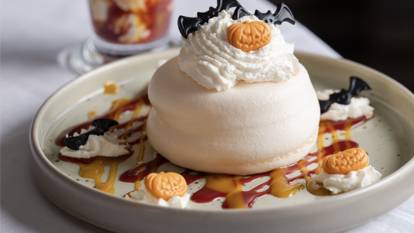 Delight in festive pavlova with whipped cream, pumpkin and bat decorations, perfect for a cosy hotel dessert experience.