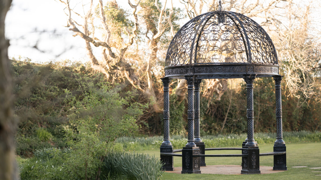 Elegant wrought-iron gazebo amidst lush garden, offering tranquil relaxation and charming views for guests.