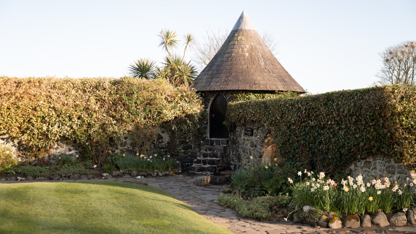 Charming stone gazebo with a conical roof, surrounded by lush gardens and daffodils, creates a tranquil escape.