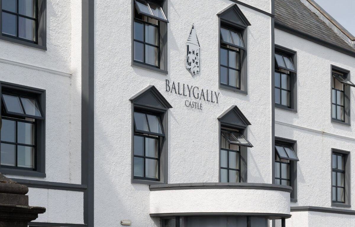 Elegant entrance of Ballygally Castle Hotel, with lush planters and inviting architecture nestled in tranquil surroundings.