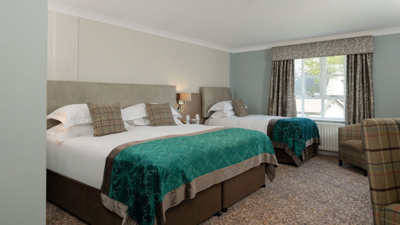 Spacious twin room with comfortable beds, elegant decor, armchair, and scenic view from window at luxury hotel.