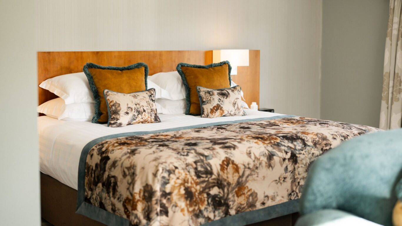 A neatly made bed with floral-patterned bedding, decorative pillows, and a wooden headboard in a softly lit bedroom.
