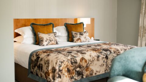 A neatly made bed with floral-patterned bedding, decorative pillows, and a wooden headboard in a softly lit bedroom.