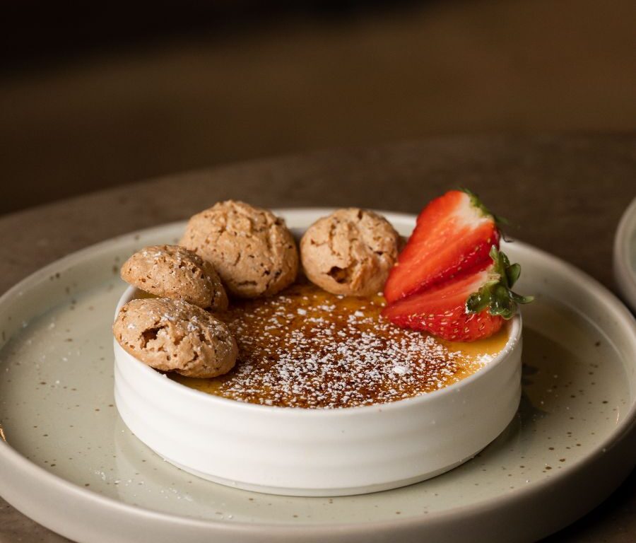 A round dessert topped with three cookies, a sliced strawberry, and powdered sugar is served on a white plate.