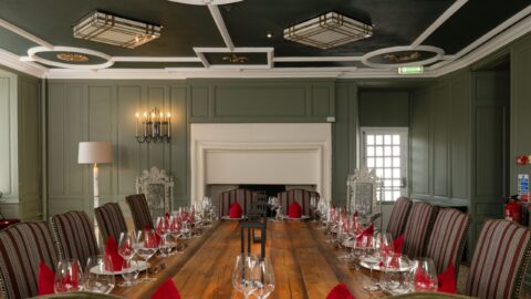 Elegant hotel dining room with long wooden table, plush chairs, ambient lighting, and set with wine glasses.
