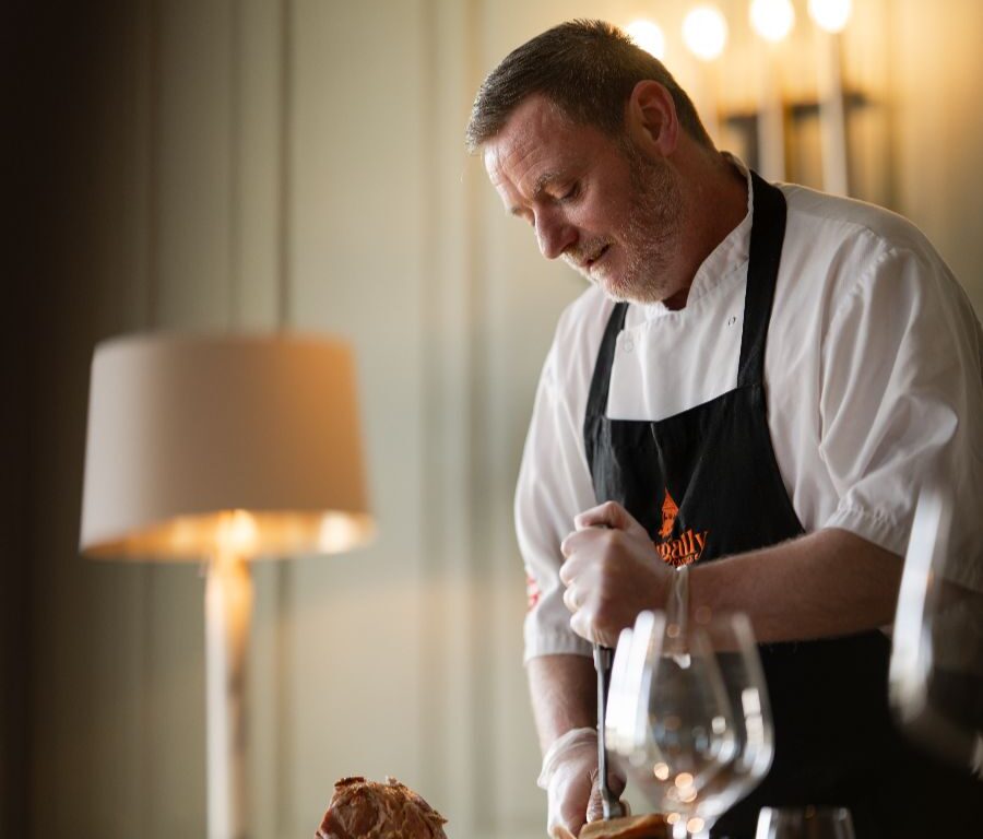Chef expertly carves roast in elegant hotel dining room, creating a warm, inviting atmosphere with refined cuisine.