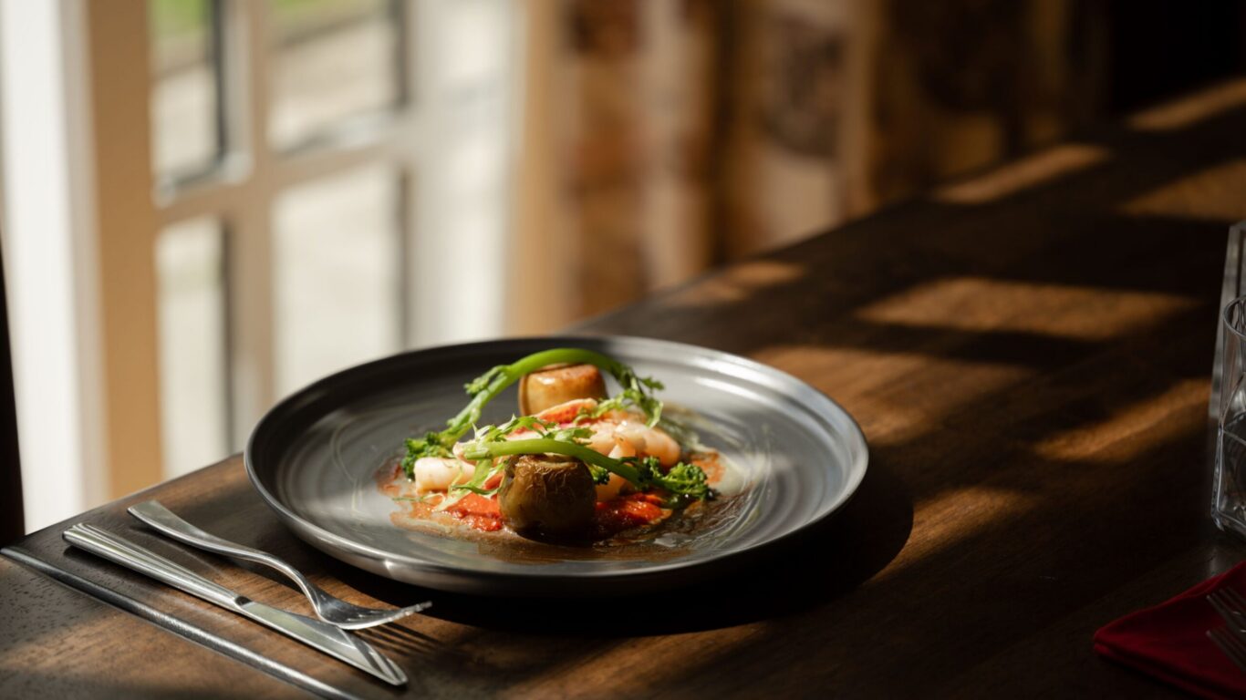 Elegant dish with scallops and fresh vegetables served in sunlit hotel dining room, showcasing gourmet restaurant.